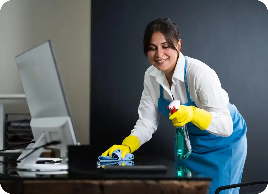 Smiling female cleaner sanitising office desk with spray and cloth — Busy B Cleaning’s reliable commercial cleaning services in Australia