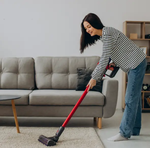Woman vacuuming living room carpet with cordless vacuum cleaner for deep home cleaning